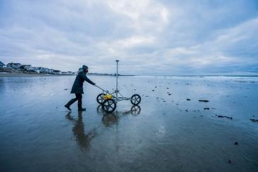Female student pushes a GPS cart across a beach in winter